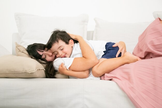 Brunette mother sleeping on couch and embracing cute son.