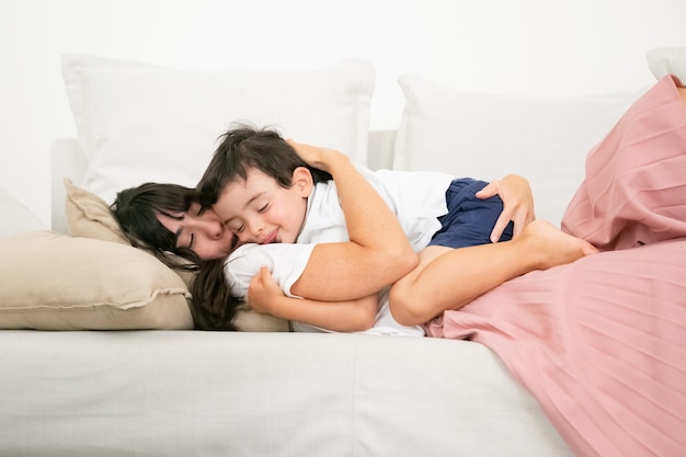 Brunette mother sleeping on couch and embracing cute son.