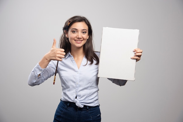 Free photo brunette painter holding canvas and giving thumbs up.