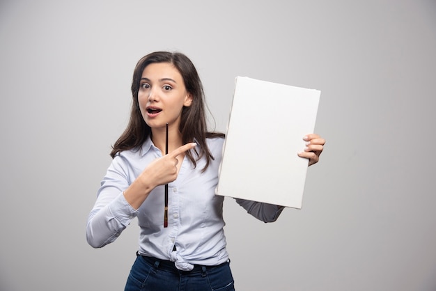 Brunette painter pointing at canvas on gray wall. 