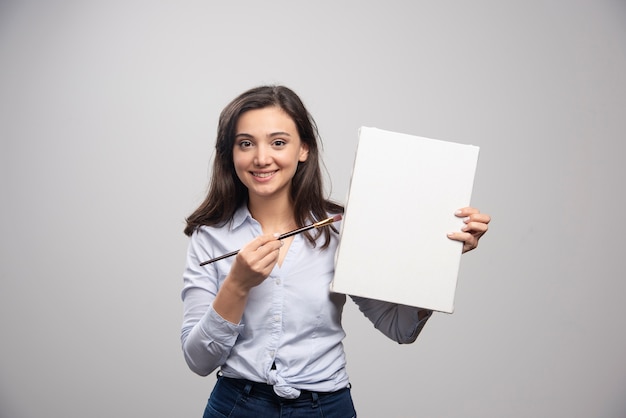 Free photo brunette painter posing with canvas and brush on gray wall.