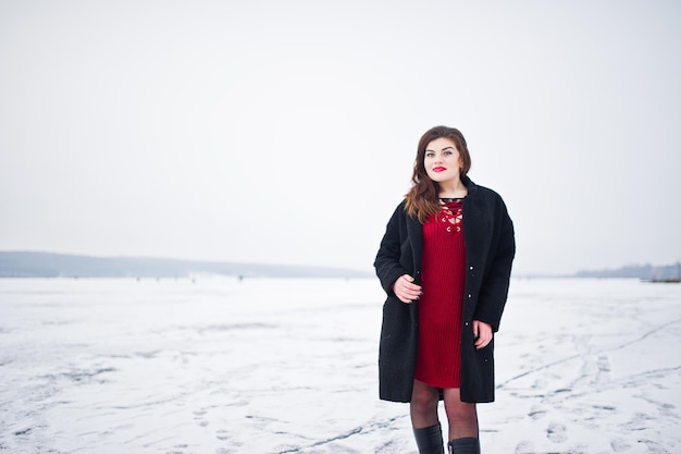 Brunette plus size model at red against frozen lake on winter day