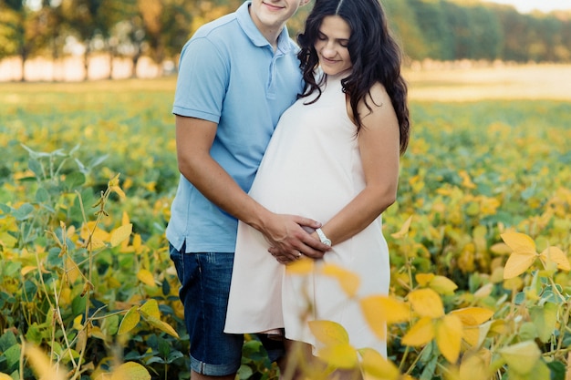 Brunette pregnant lady hugs with her man on yellow field 