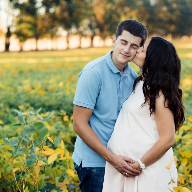 Brunette pregnant lady kisses her man while they stand on the field 