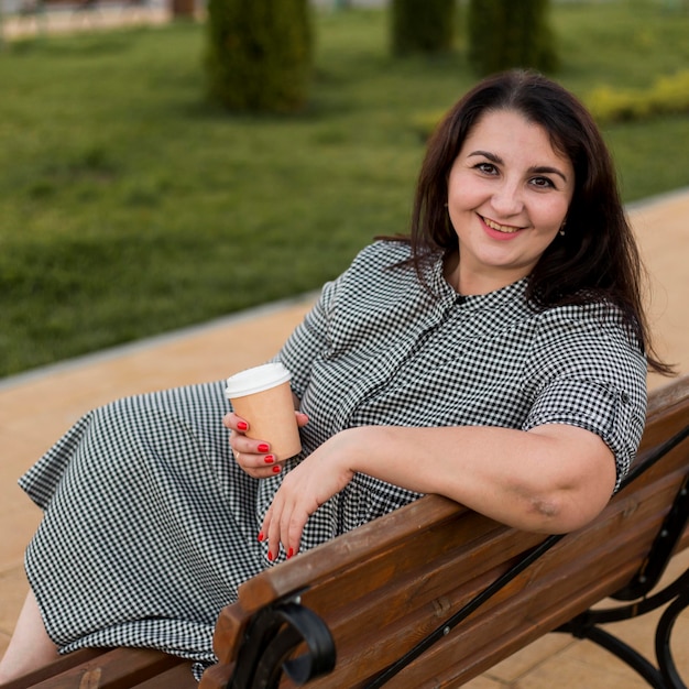 Foto gratuita donna castana di smiley che tiene una tazza di caffè all'esterno