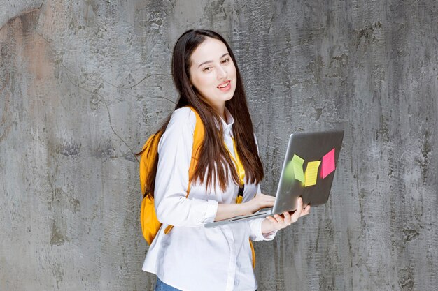 Brunette student standing and holding laptop. High quality photo