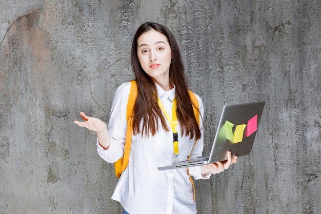 Brunette student standing and holding laptop. High quality photo