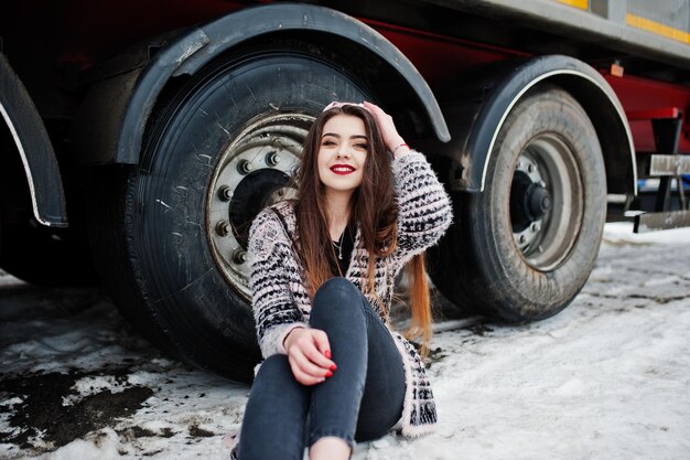 Brunette stylish casual girl in cap sitting against truck wheels