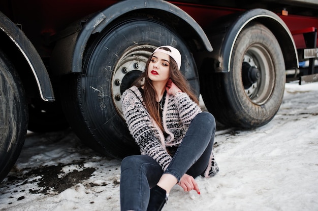 Free photo brunette stylish casual girl in cap sitting against truck wheels