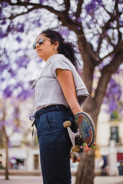 Brunette teenage girl holding skateboard standing outside