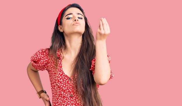 Brunette teenager girl wearing summer dress doing italian gesture with hand and fingers confident expression