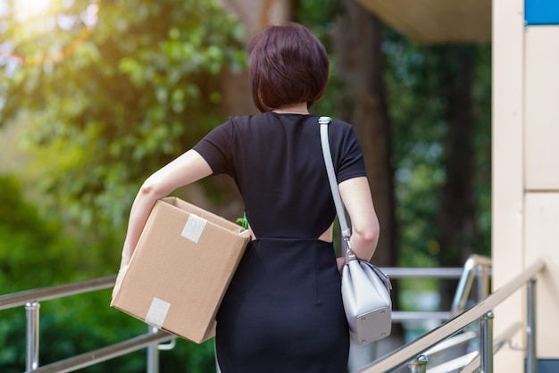 Brunette with a chic figure with a box of personal items, rear view.