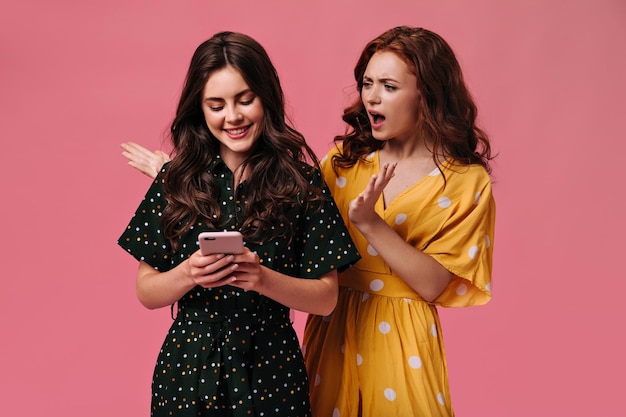 Brunette woman chatting on phone while her friend judgingly looking at her Beautiful girl in yellow doesnt like that lady in black looking at phone
