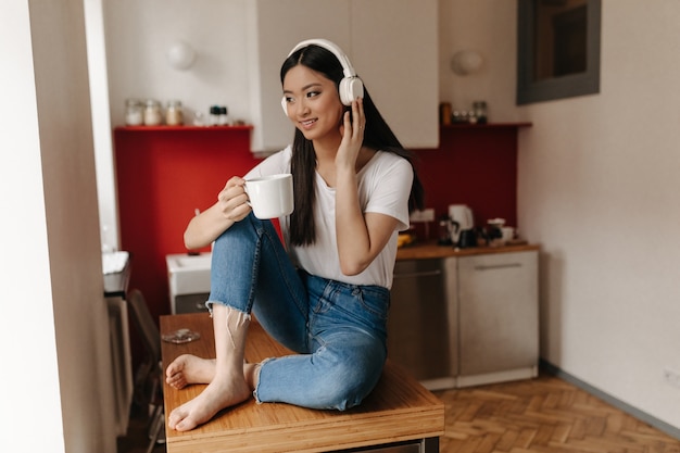 Brunette woman dressed in jeans and top posing against background of kitchen