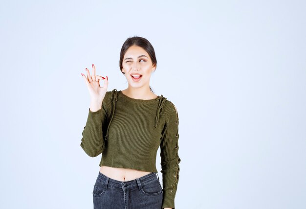 brunette woman giving thumbs up with one eye closed on white background.