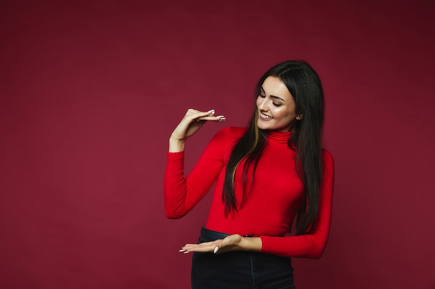 Brunette woman has happy look and showing something standing on a claret color 