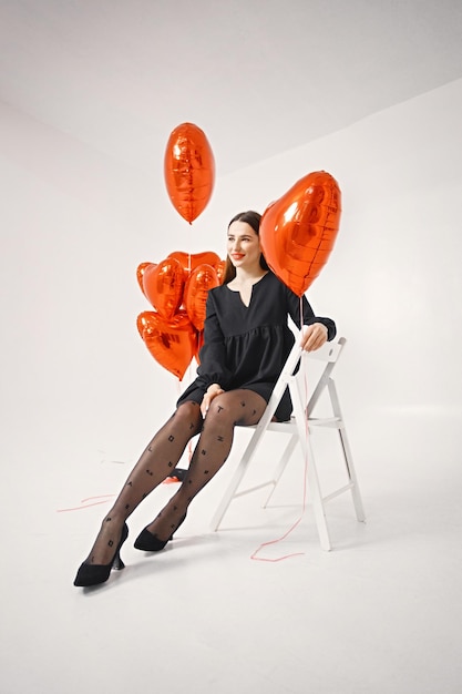 Brunette woman holding a bunch of heartshaped red balloons in studio