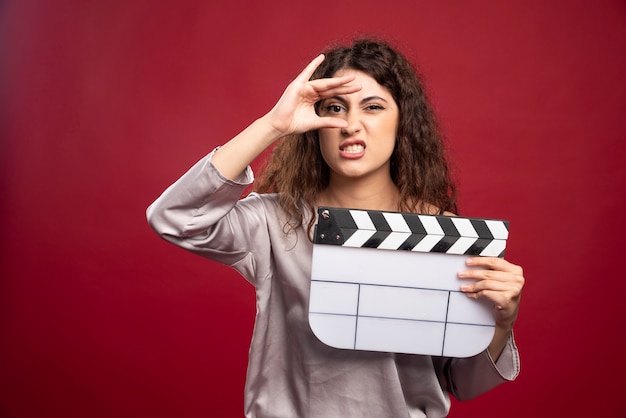 Brunette woman holding clapperboard and making faces.