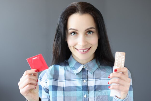 Brunette woman holding condom and birth control pills choosing contraception for unwanted