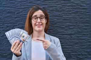 Free photo brunette woman holding dollars smiling happy pointing with hand and finger