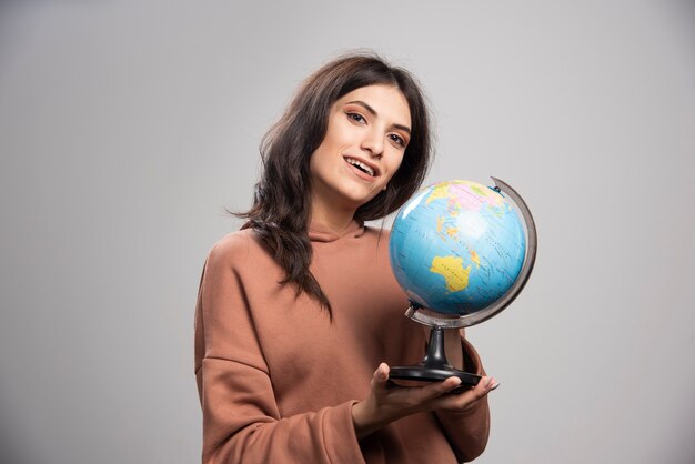 Brunette woman holding globe on gray