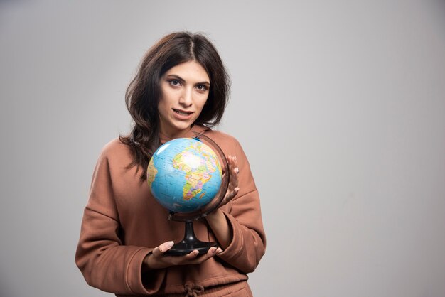 Brunette woman holding globe on gray