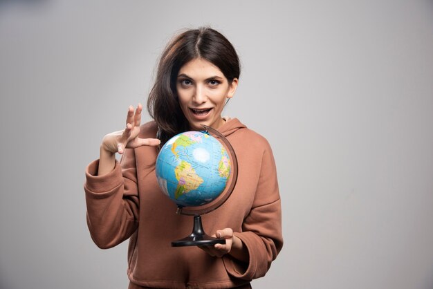 Brunette woman holding globe on gray