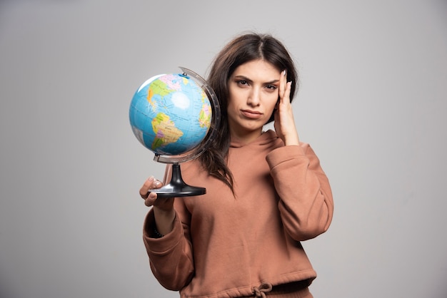 Brunette woman holding globe on gray