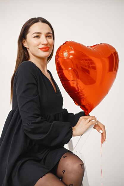 Brunette woman holding a heartshaped red balloon and posing in studio