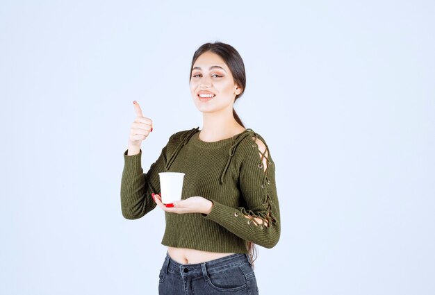 brunette woman holding plastic cup and giving thumbs up.