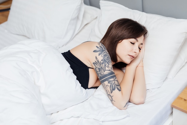 ブルネットの女性は、朝目を覚ます彼女の腕と体を伸ばしてベッドに横になります