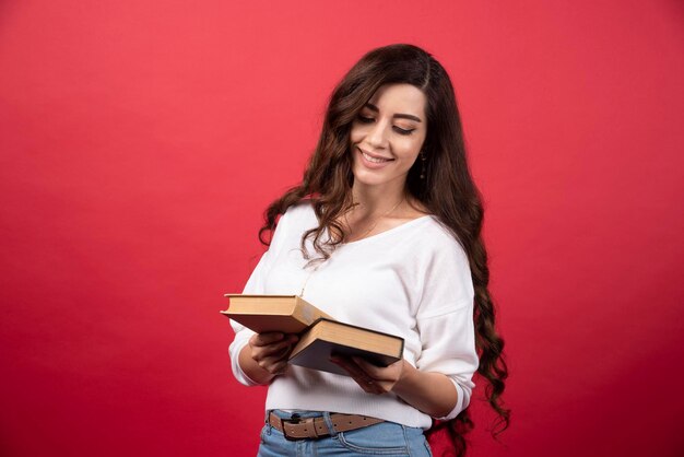 Brunette woman looking at books on red background. High quality photo