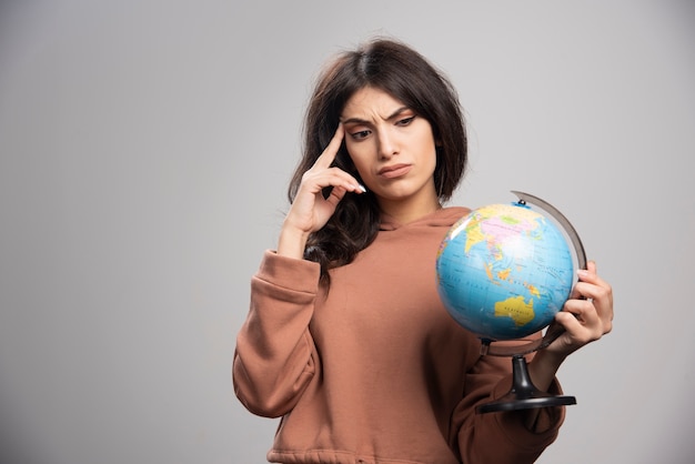 Brunette woman looking at globe on gray