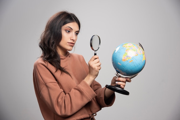 Brunette woman looking at globe with magnifying glass