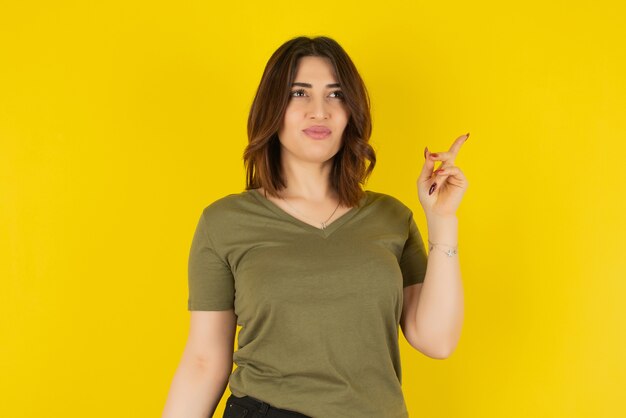 Brunette woman model standing and pointing up against yellow wall 