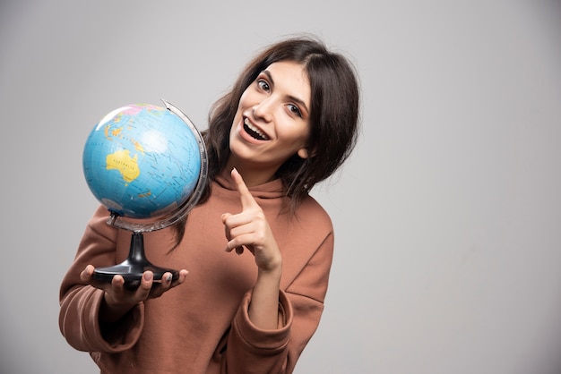 Brunette woman pointing at globe on gray