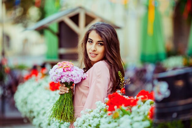 ブルネット女の子が花瓶の中にピンクの花束でポーズをとる