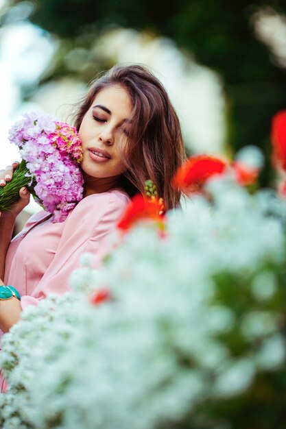 Брюнетка женщина позирует с розовым букетом среди цветочных горшков