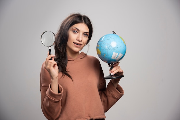 Brunette woman posing with magnifying glass and globe