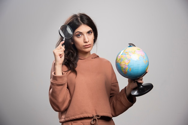 Brunette woman posing with magnifying glass and globe