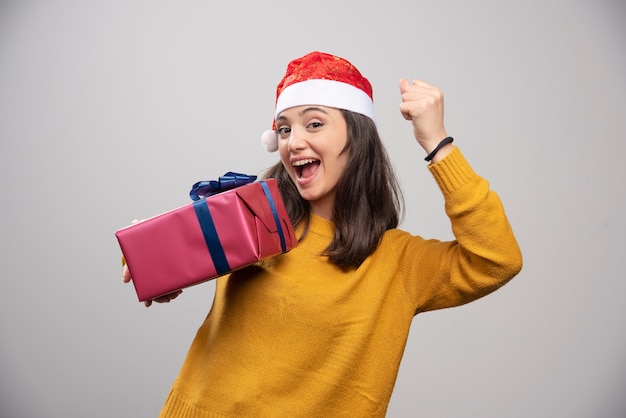 Donna castana in cappello della santa che mostra il suo pugno e che tiene il contenitore di regalo.