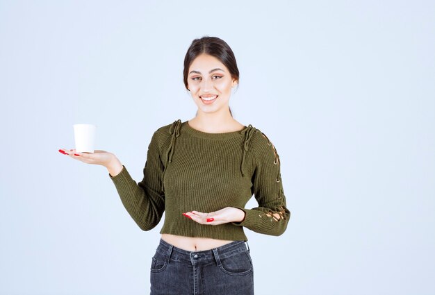 brunette woman showing plastic cup on white background.