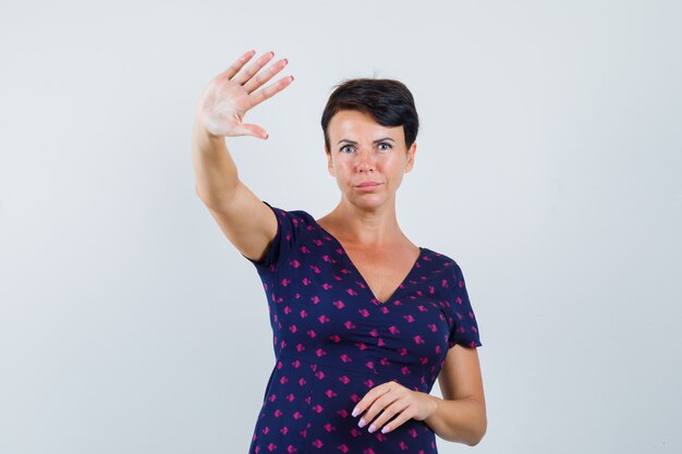 Брюнетка женщина показывает отказ или знак остановки в фиолетовом и красном платье с рисунком и выглядит серьезным, вид спереди.