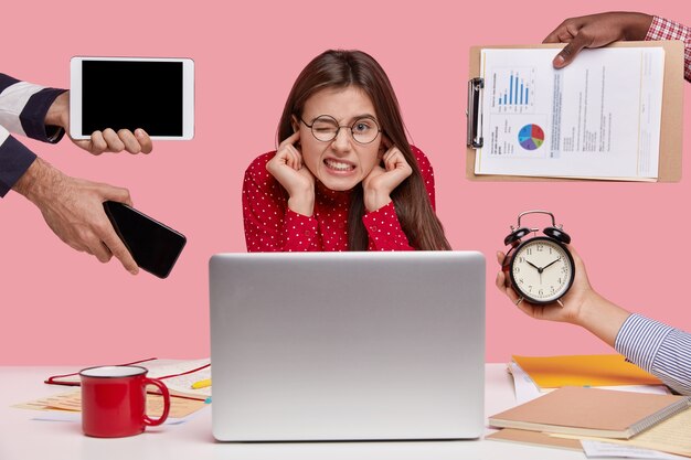 Brunette woman sitting at desk surrounded with gadgets and papers