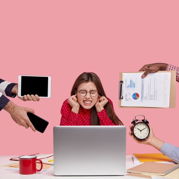 Brunette woman sitting at desk surrounded with gadgets and papers