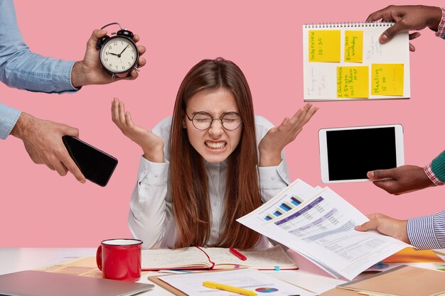 Brunette woman sitting at desk surrounded with gadgets and papers