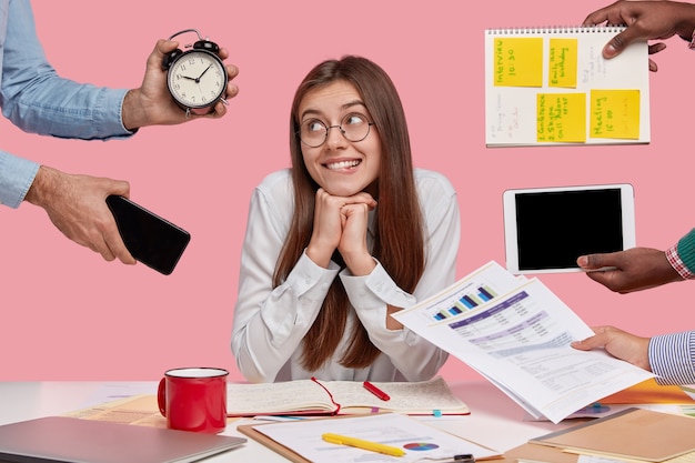 Brunette woman sitting at desk surrounded with gadgets and papers