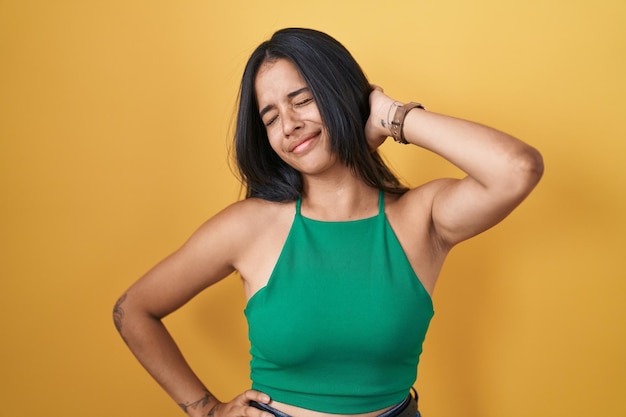 Free photo brunette woman standing over yellow background suffering of neck ache injury touching neck with hand muscular pain