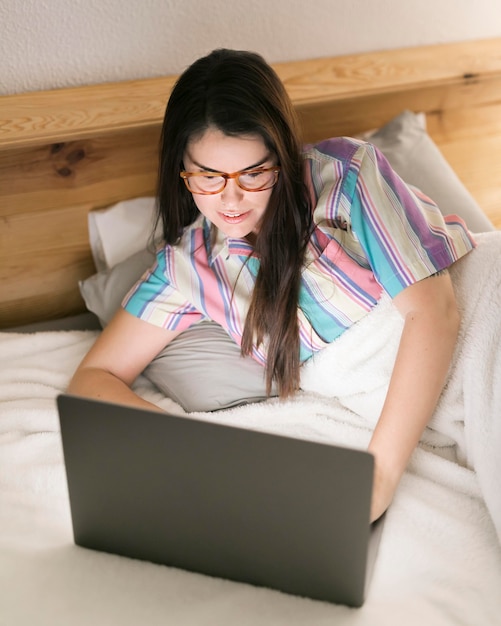 Free photo brunette woman staying in bed and working on laptop