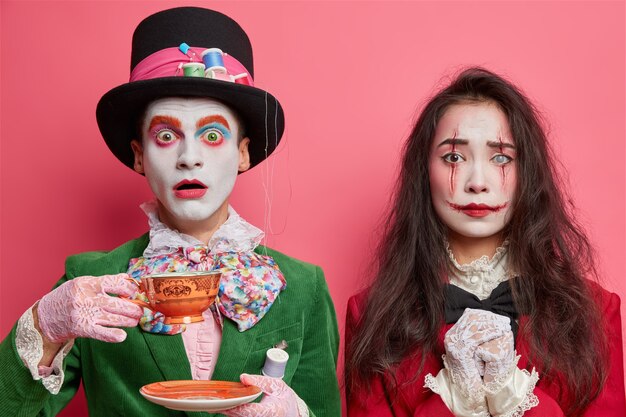 brunette woman wears makeup of ghost vampire or zombie for halloween has bloody lips and scars on face isolated over rosy studio wall